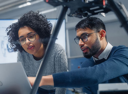 two colleagues looking at drone software on laptop with drone on desk