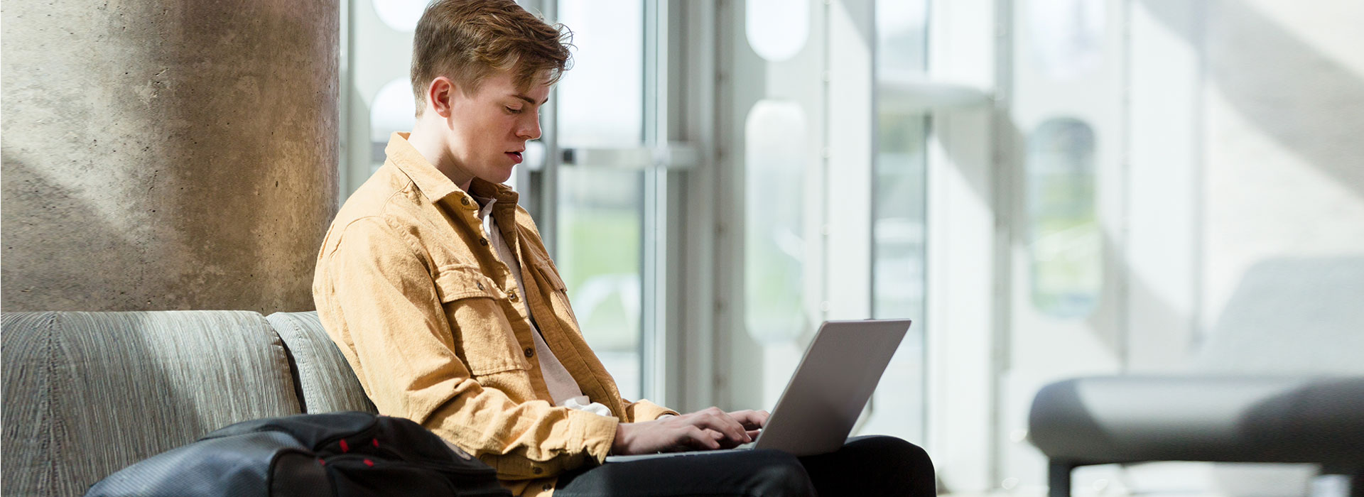 younger male Student at a laptop computer holding book